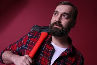 Lumberjack with axe looking away while standing against red background