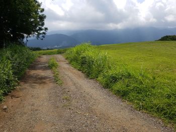 Dirt road amidst field against sky