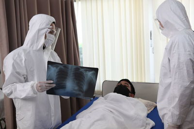 Doctors explaining medical x-ray to patient lying on bed in hospital ward