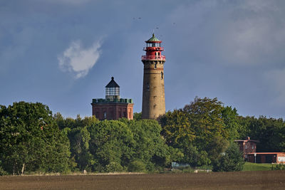 Lighthouse amidst trees and buildings against sky