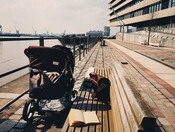 Book and bag on bench by baby carriage in city