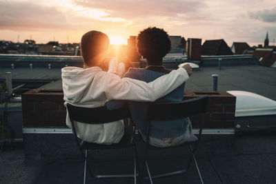 Rear view of couple sitting on seat at sunset
