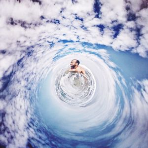 Little planet format view of man in sea against cloudy sky