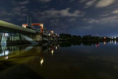 Illuminated building by river against sky at night