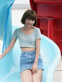 Portrait of smiling young woman standing against wall