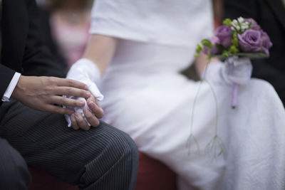 Midsection of bride and groom holding hands and flower bouquet