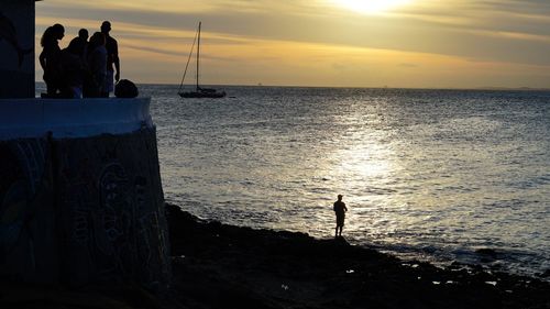 Silhouette people standing on beach against sky during sunset