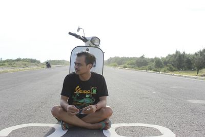 Full length of boy sitting on road against sky