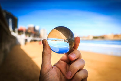 Close-up of hand holding sunglasses against blue sky