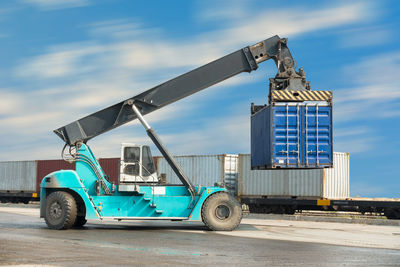 Crane lifting cargo container at dock against sky