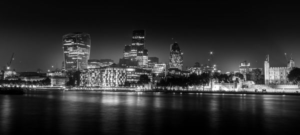 Illuminated buildings by river against sky at night