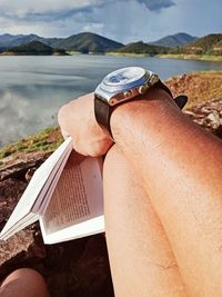 Midsection of person by sea against mountain