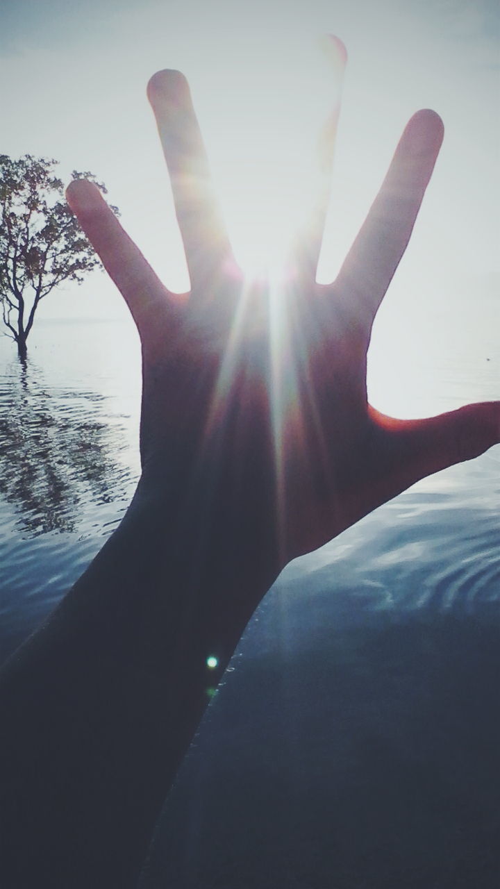 CLOSE-UP OF HANDS AGAINST SUN SHINING IN WATER