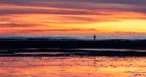 Scenic view of beach against dramatic sky during sunset