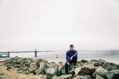 Man sitting on rock by sea against sky