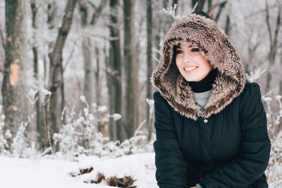 Woman wearing fur coat standing against trees during winter