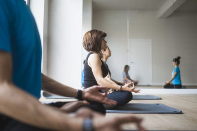 Mirror reflection of group of people with female instructor practicing yoga meditation in lotus pose with mudra hands during class in studio