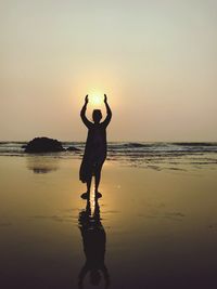 Optical illusion of silhouette woman holding sun while standing at beach