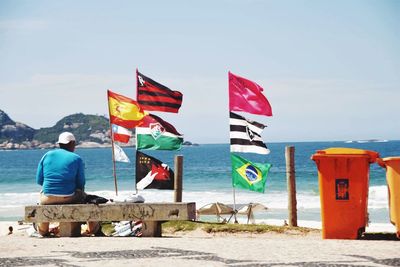 Rear view of man sitting on seat with various flags at beach