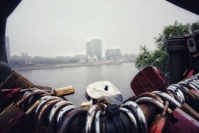 Padlocks on bridge over river against sky in city