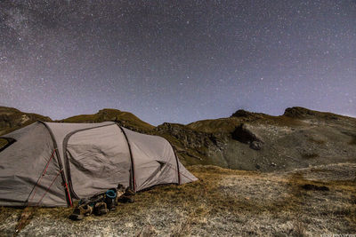 Shoes by tent on field against constellation at night