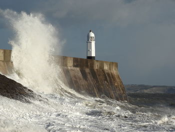 Lighthouse and huge wave by sea against sky