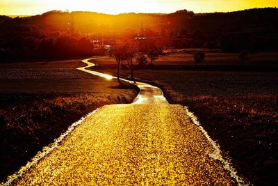 Road by trees against sky during sunset