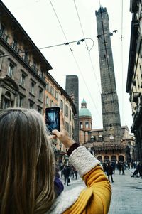 Cropped hand of woman photographing bologna tower in city