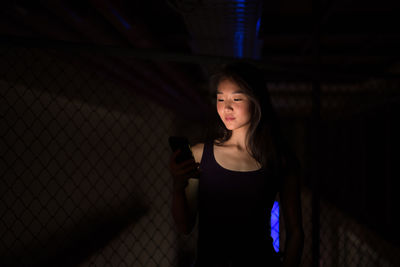 Portrait of young woman using phone while standing at night