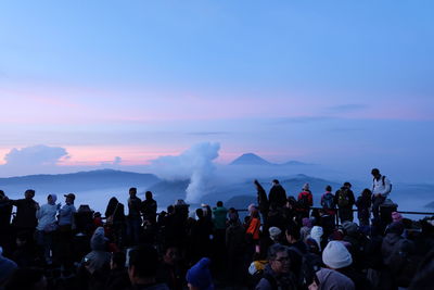 Group of people on shore against sky during sunset