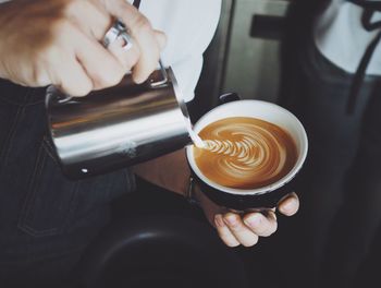 Cropped image of person making froth art on cappuccino