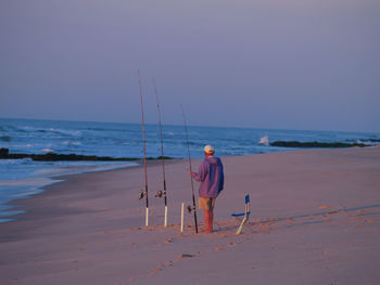 Rear view of man fishing at beach against clear sky