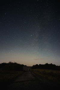 Road amidst silhouette landscape against star field at night