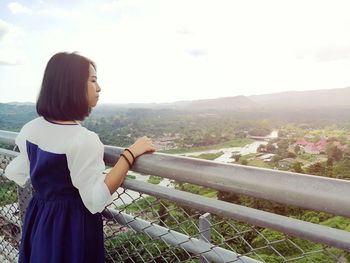 Side view of woman standing on railing against sky