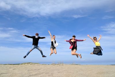 Happy friends jumping at beach against blue sky