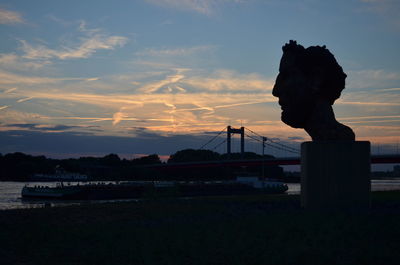 Silhouette sculpture and bridge against sky at dusk