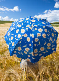 Woman with umbrella on field against blue sky