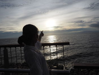 Woman standing by railing against sea during sunset