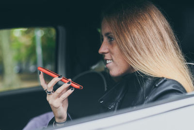 Trendy girl sitting in a car. teen recording voice message with smartphone. woman chat with friends