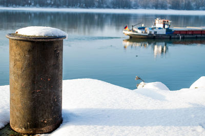 Close-up of bollard amidst snow against river during winter