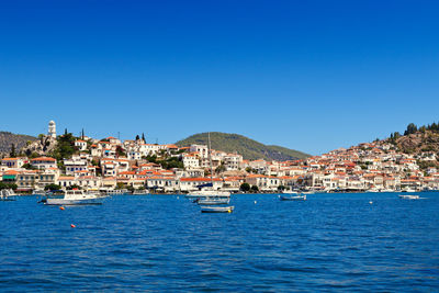 Sailboats in sea by town against clear blue sky