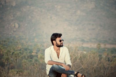 Young man looking away while sitting on land