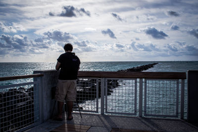 Rear view of man standing on pier over sea