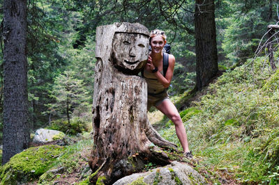 Full length of woman in tree trunk amidst plants in forest