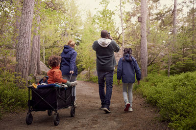 Mother pulling son sitting on cart while walking with man and daughter in forest