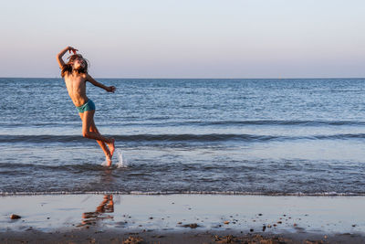 Full length of man jumping on beach against sky