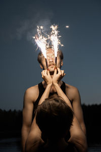 Midsection of woman holding sparkler against sky