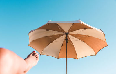 Low section of woman with parasol against clear blue sky