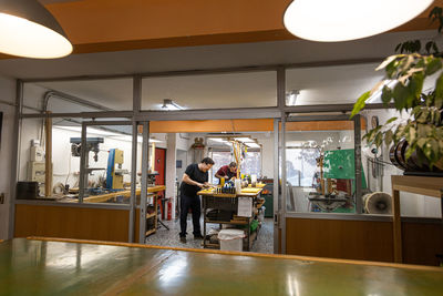 Focused craftsmen luthiers working in own workshop repairing electric guitars with different professional equipment and glass walls