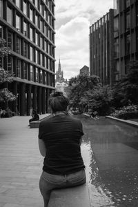 Rear view of woman by buildings in city against sky